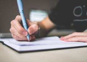 Close-up of hand writing in notebook using a blue pen, focus on creativity.