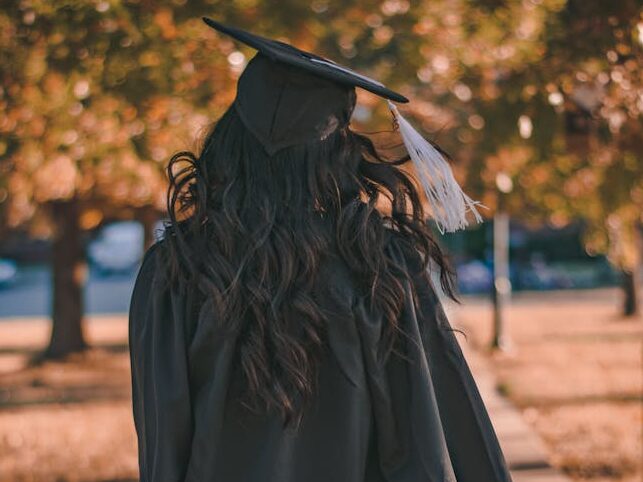 Back view of a graduate walking in an autumn park in academic dress.