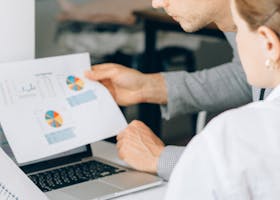 Two business professionals reviewing financial charts and graphs in a modern office setting.